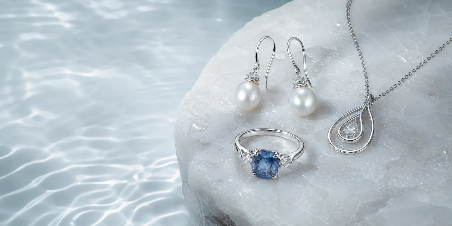 Freshwater pearl earrings, blue gemstone ring, and silver necklace arranged on pearl-white stone