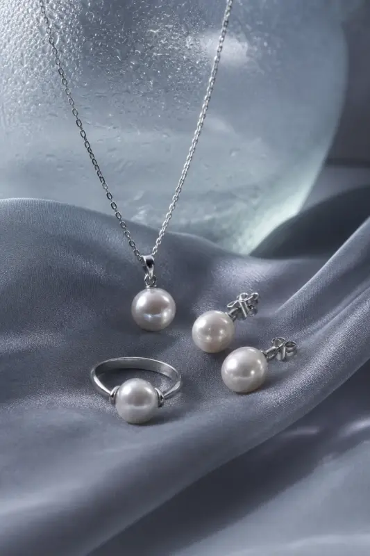 Freshwater pearl necklace, earrings, and ring resting on cool gray silk